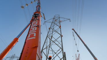 The conductor cables have been removed from the insulators and suspended in pulleys from the cranes